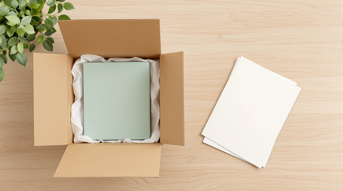 Open kraft mailer box with tissue paper and a sage green printed product box inside, blank insert cards beside it